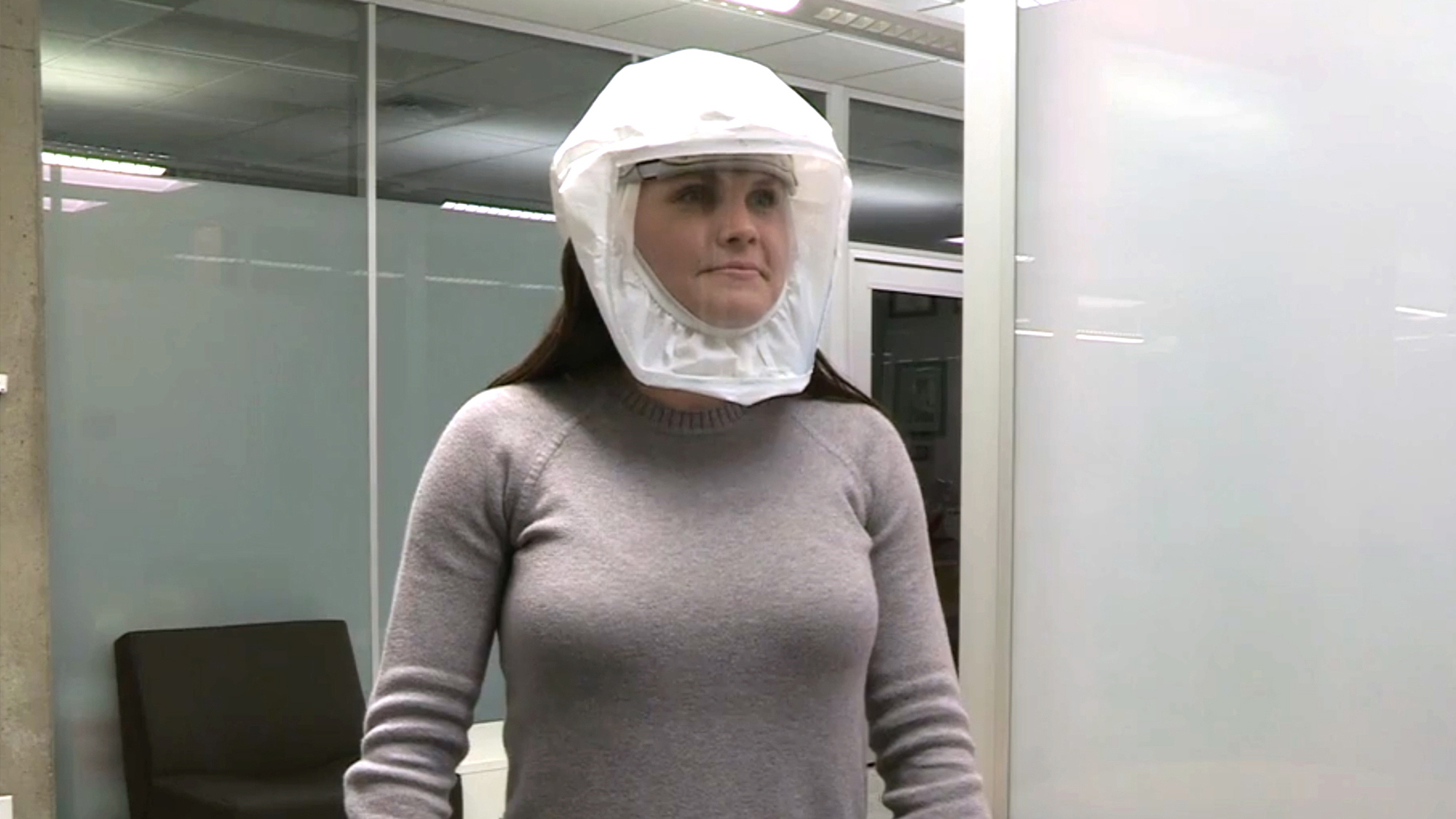A woman in a face shield with a gray long sleeve shirt.