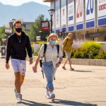 Two students walk on the University of Utah campus, both wearing masks.